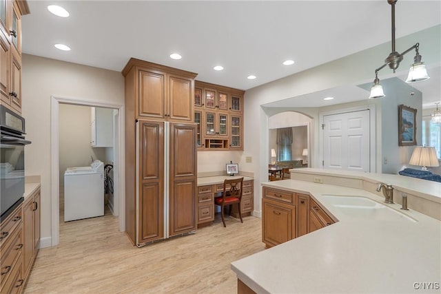 kitchen featuring a sink, brown cabinets, light wood finished floors, washer and clothes dryer, and light countertops