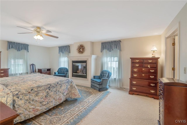 carpeted bedroom featuring a glass covered fireplace and a ceiling fan