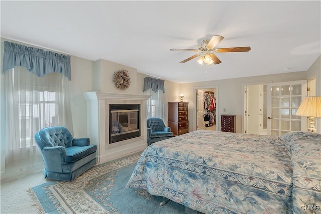 bedroom featuring a walk in closet, a tiled fireplace, ceiling fan, and a closet