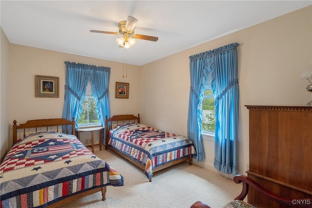 bedroom featuring multiple windows, light carpet, a ceiling fan, and baseboards