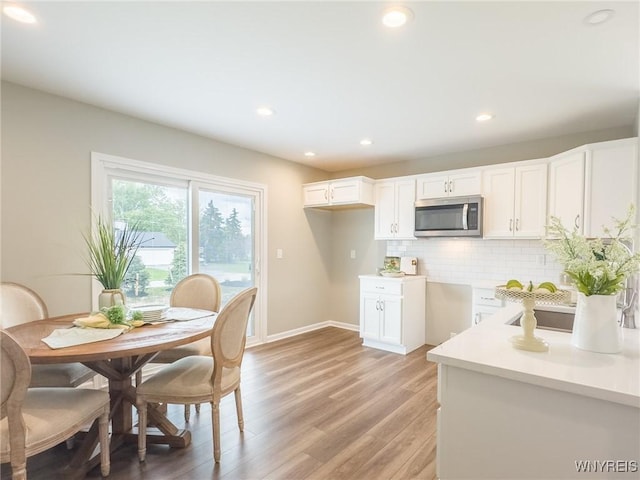 kitchen featuring stainless steel microwave, decorative backsplash, light wood finished floors, recessed lighting, and white cabinetry