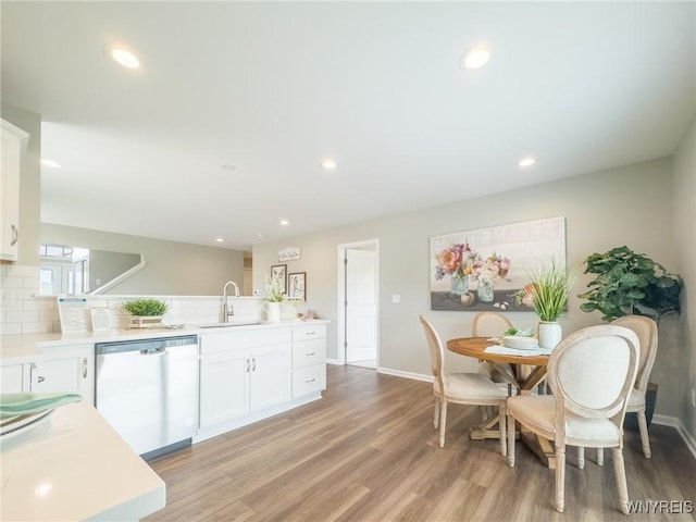 kitchen with dishwasher, a sink, light wood finished floors, backsplash, and white cabinetry