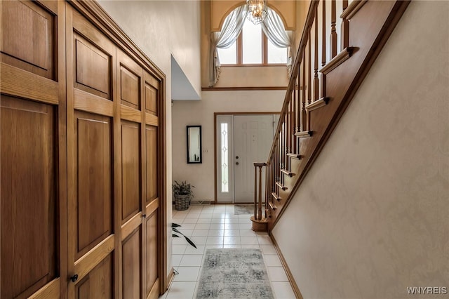 foyer entrance with light tile patterned flooring, a towering ceiling, stairs, a chandelier, and baseboards
