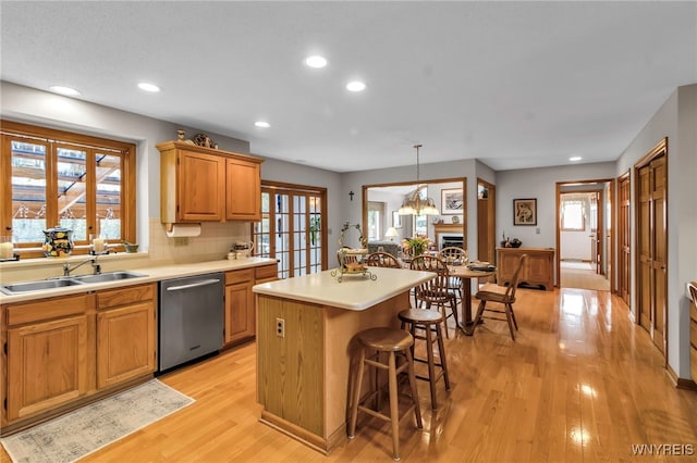 kitchen featuring dishwasher, a sink, a kitchen island, light wood-type flooring, and light countertops