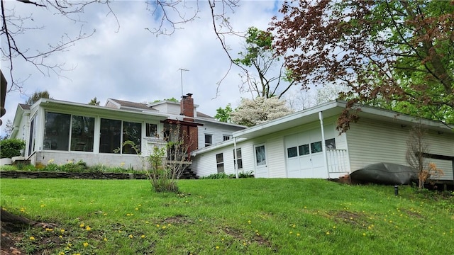 back of property featuring a sunroom, an attached garage, a lawn, and a chimney