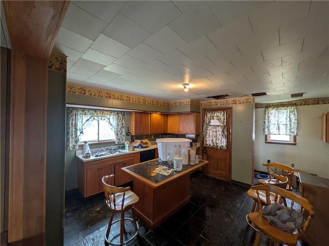 kitchen with brown cabinetry, a sink, healthy amount of natural light, and a center island