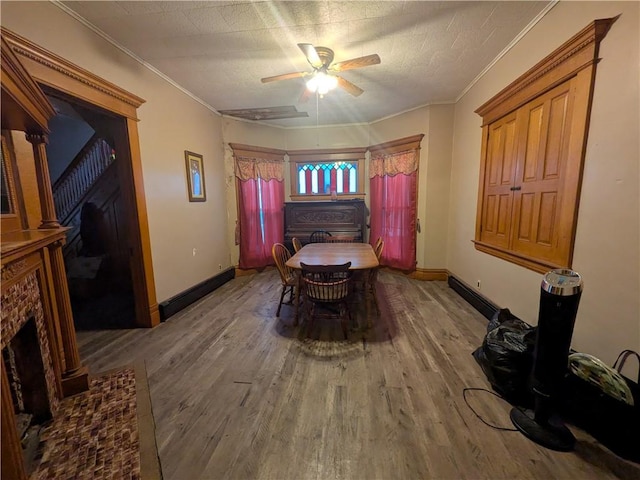dining room with wood finished floors, a ceiling fan, a fireplace, baseboards, and crown molding