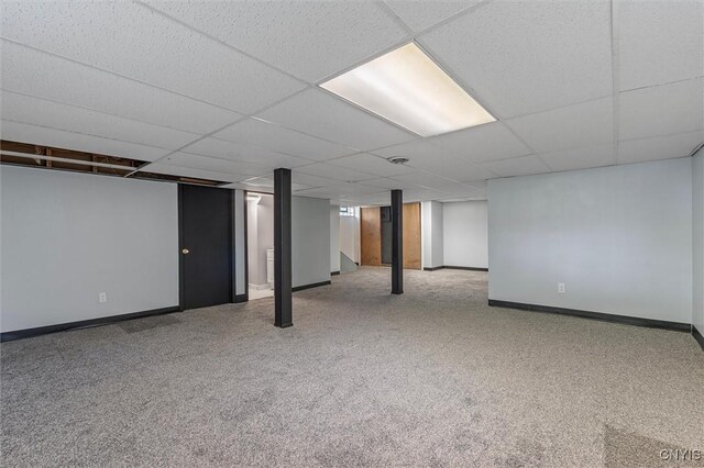 finished basement with baseboards, a drop ceiling, and carpet floors