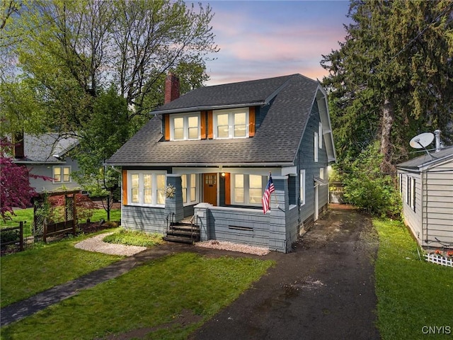 view of front facade featuring a chimney, a front lawn, driveway, covered porch, and a shingled roof