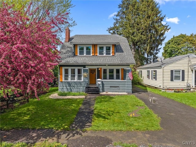 view of front of home featuring a chimney, a front lawn, and a shingled roof