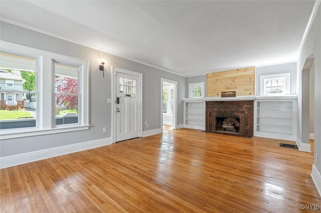 unfurnished living room featuring wood finished floors, ornamental molding, baseboards, and a brick fireplace