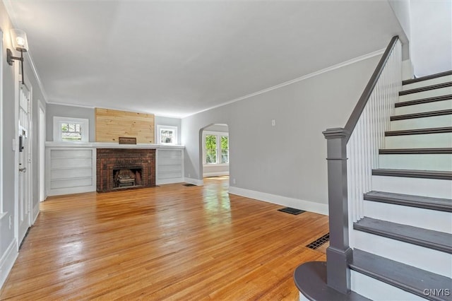 unfurnished living room with arched walkways, light wood-type flooring, stairway, baseboards, and crown molding