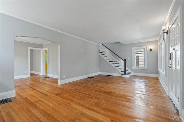 foyer entrance featuring stairway, arched walkways, baseboards, light wood-type flooring, and crown molding