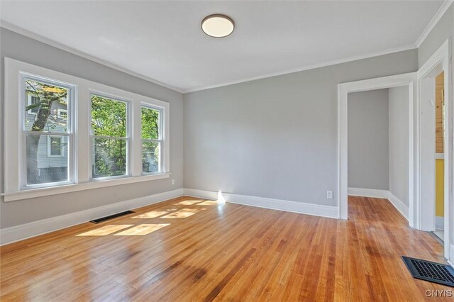 empty room with ornamental molding, light wood-type flooring, and baseboards