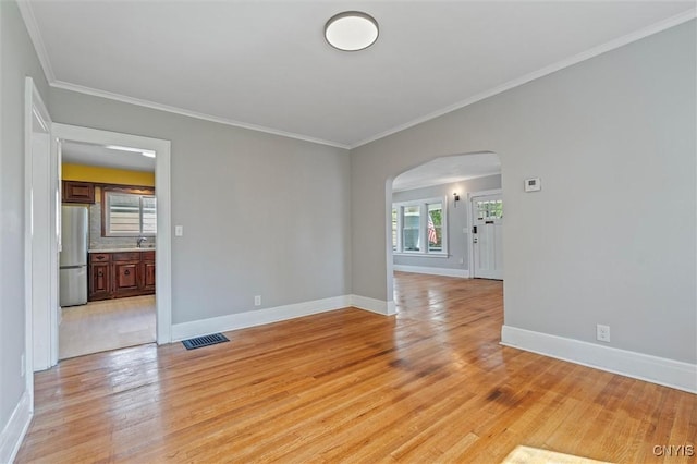 spare room featuring arched walkways, crown molding, light wood-type flooring, and baseboards