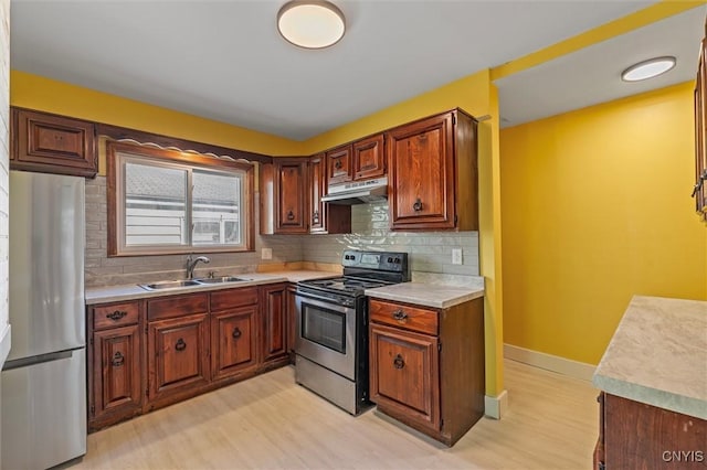 kitchen with appliances with stainless steel finishes, a sink, under cabinet range hood, light countertops, and tasteful backsplash