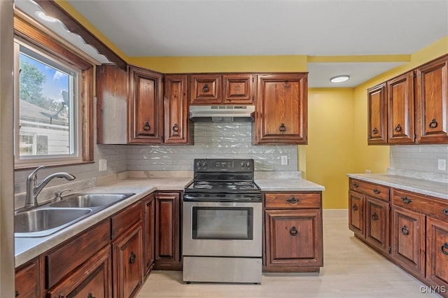 kitchen featuring electric range, a sink, under cabinet range hood, light countertops, and backsplash
