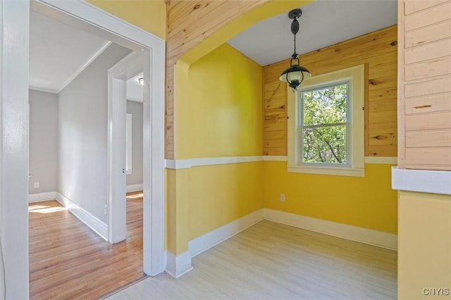 empty room featuring wood finished floors, crown molding, baseboards, and wooden walls