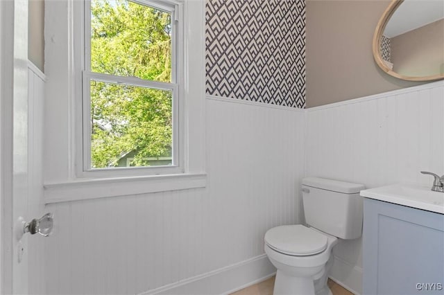 half bath featuring toilet, vanity, and a wainscoted wall
