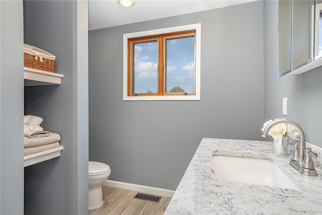 half bathroom featuring wood finished floors, toilet, baseboards, and vanity