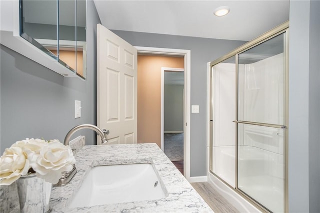 full bathroom with a stall shower, vanity, baseboards, and wood finished floors