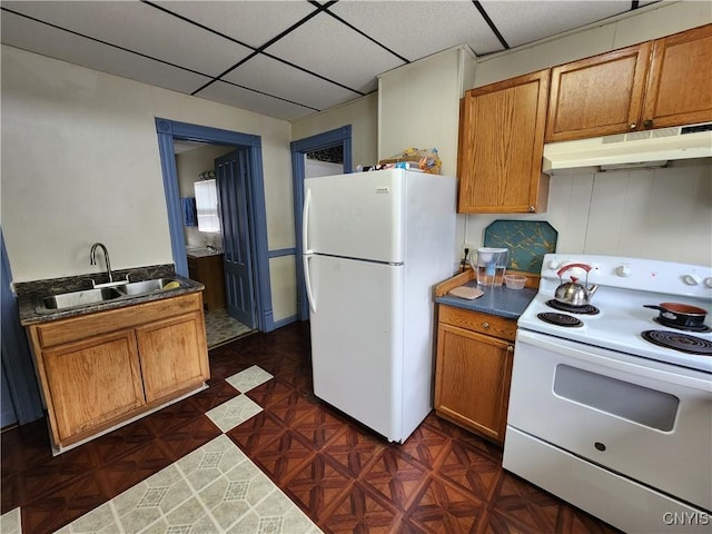 kitchen with white appliances, under cabinet range hood, a sink, brown cabinetry, and a paneled ceiling