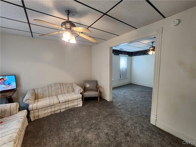 living area with dark carpet, ceiling fan, a paneled ceiling, and baseboards