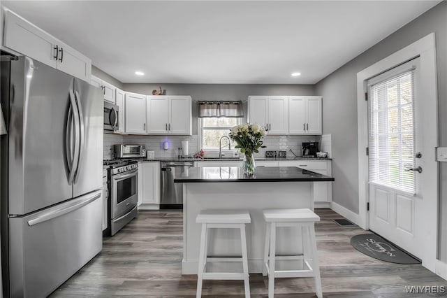 kitchen featuring stainless steel appliances, dark countertops, backsplash, a kitchen island, and recessed lighting