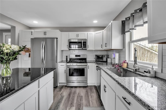 kitchen featuring appliances with stainless steel finishes, a sink, dark stone countertops, light wood-type flooring, and white cabinets