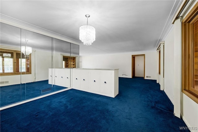 empty room with a chandelier, dark colored carpet, and ornamental molding