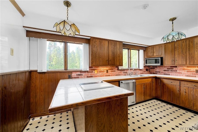 kitchen featuring stainless steel appliances, a sink, tile countertops, light floors, and brown cabinetry