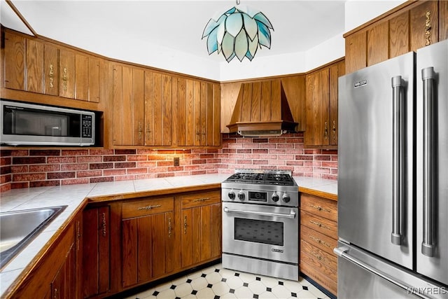 kitchen with high quality appliances, custom range hood, tile countertops, and brown cabinets