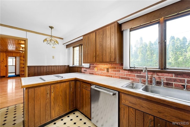 kitchen with stainless steel dishwasher, light flooring, brown cabinetry, tile counters, and wooden walls