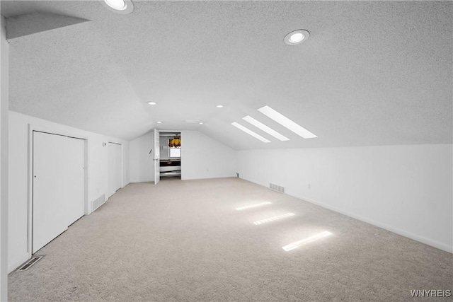 additional living space with light carpet, vaulted ceiling, a textured ceiling, recessed lighting, and a skylight