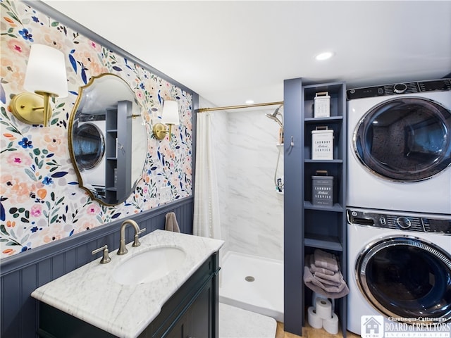 bathroom with stacked washing machine and dryer, a stall shower, wainscoting, wallpapered walls, and vanity