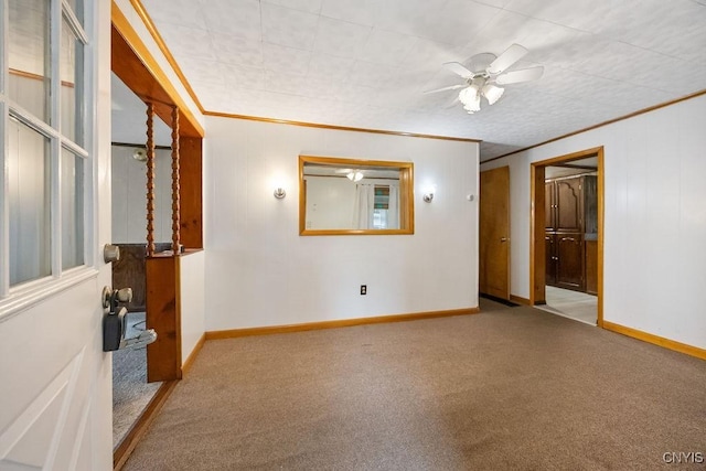 carpeted empty room with ornamental molding, a ceiling fan, and baseboards