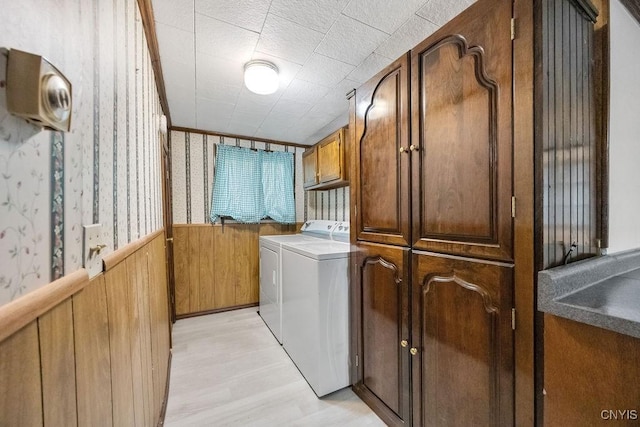 laundry room with cabinet space, washer and clothes dryer, wallpapered walls, light wood-style floors, and a wainscoted wall