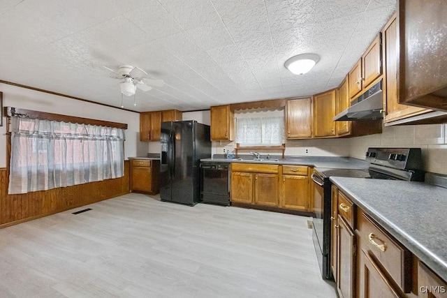 kitchen featuring under cabinet range hood, black appliances, brown cabinetry, a ceiling fan, and light wood finished floors
