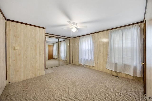 unfurnished bedroom with carpet floors, wooden walls, and ceiling fan