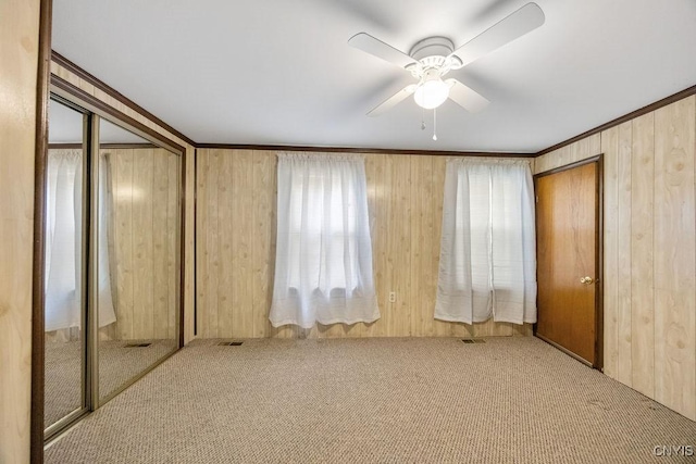 unfurnished bedroom featuring carpet floors, wooden walls, crown molding, a ceiling fan, and a closet