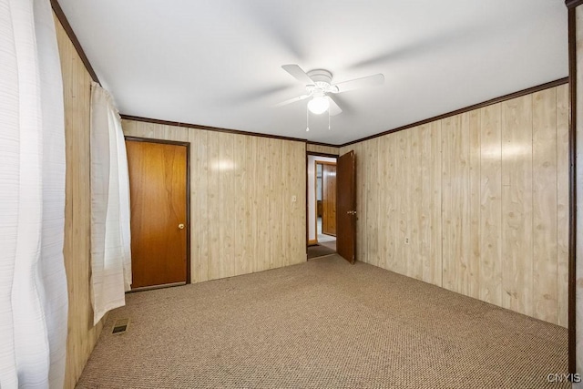 carpeted empty room featuring a ceiling fan, wood walls, and ornamental molding