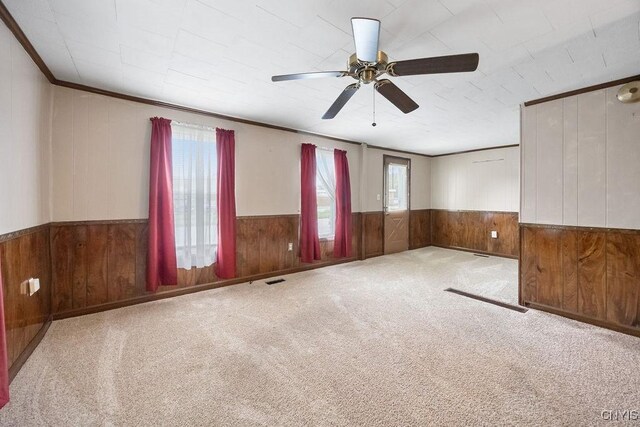unfurnished room featuring wooden walls, a wainscoted wall, ceiling fan, and carpet flooring
