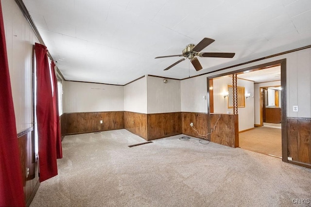 carpeted empty room featuring ceiling fan, wood walls, and wainscoting