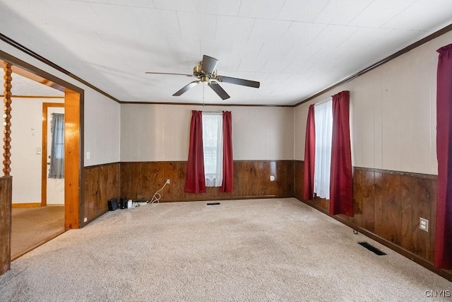 unfurnished room featuring wood walls, crown molding, a ceiling fan, carpet flooring, and wainscoting