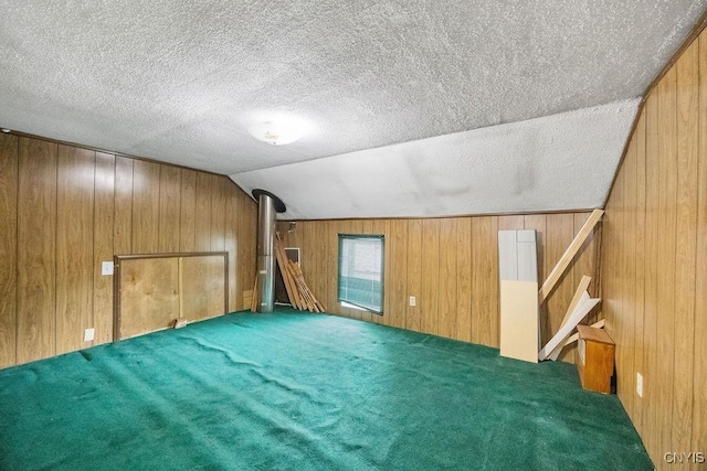bonus room with wood walls, vaulted ceiling, a textured ceiling, carpet flooring, and stairs