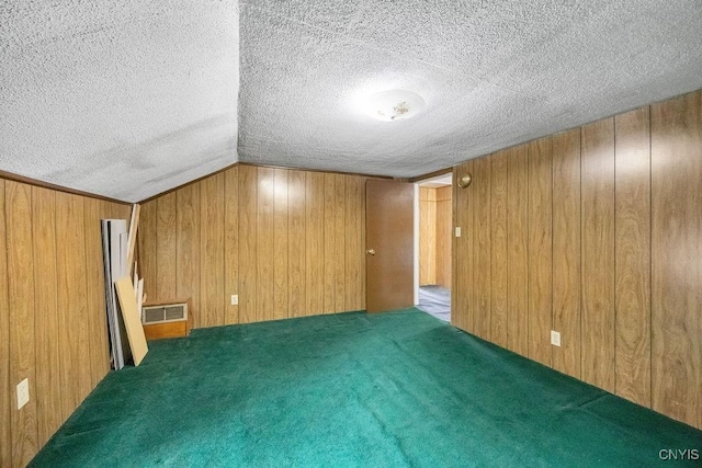 unfurnished room with a textured ceiling, wooden walls, vaulted ceiling, and carpet floors