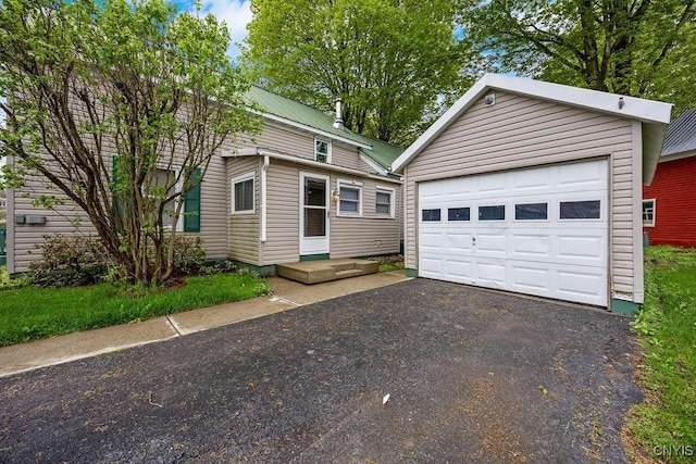 view of front facade with a detached garage, metal roof, and driveway