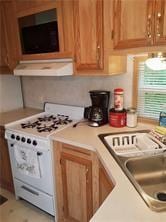 1984-2008 S Genesee St, Montour, NY 14865 - kitchen with white range with gas cooktop, under cabinet range hood, light countertops, a sink, and brown cabinetry