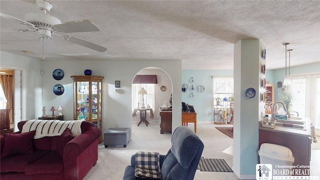 carpeted living room with a ceiling fan, a sink, a textured ceiling, and arched walkways