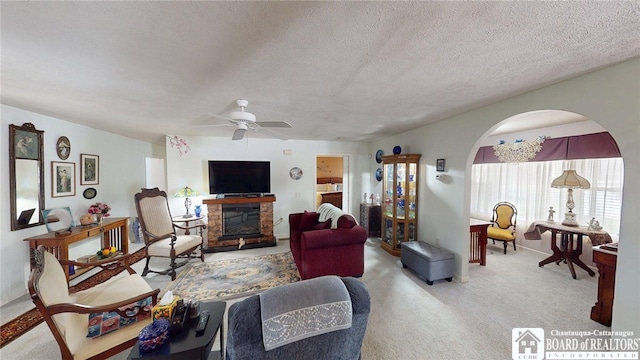 living area with a fireplace, ceiling fan, carpet, and a textured ceiling